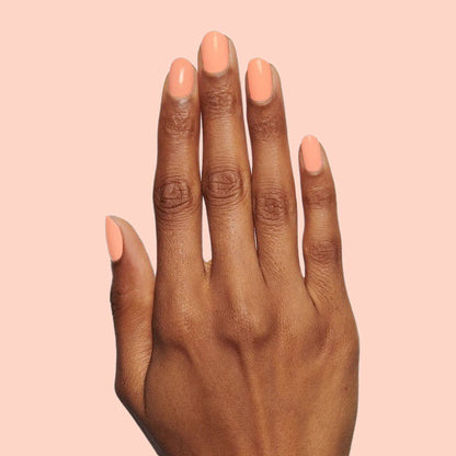 Hand with nails polished in warm coral shade Wild & Free for a vibrant at-home manicure or quick dry polish look