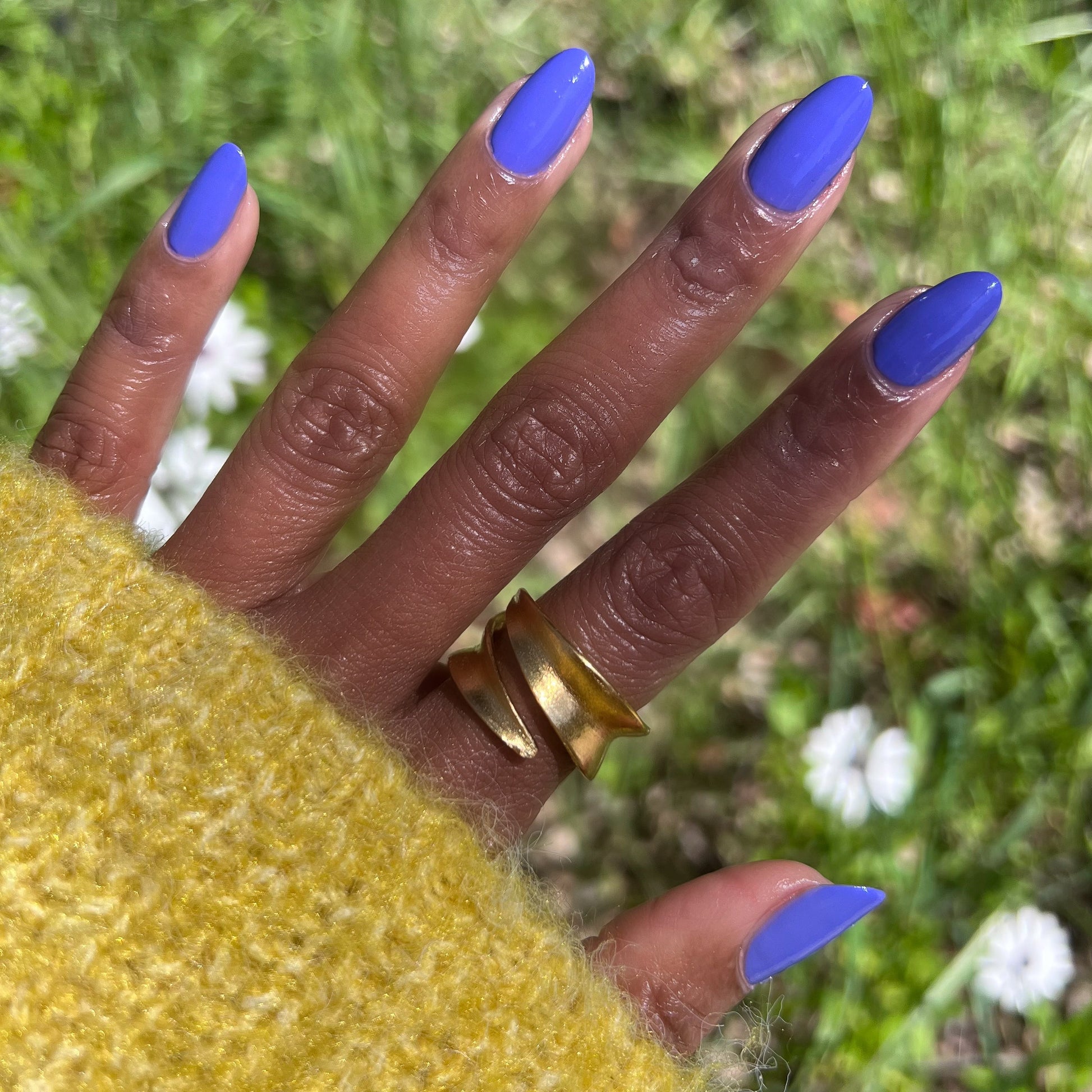 Hand with Royal quick dry gel polish in vibrant blue-purple on natural nails outdoors with green grass and white flowers background