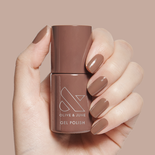 Hand holding Fawn - Gel polish bottle with matching brown neutral gel mani on a beige background