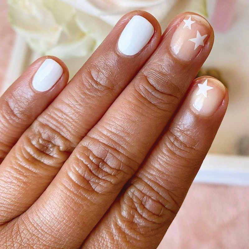 Hand with nails painted in crisp white HD polish and accent nails with stars for a stylish at-home manicure look