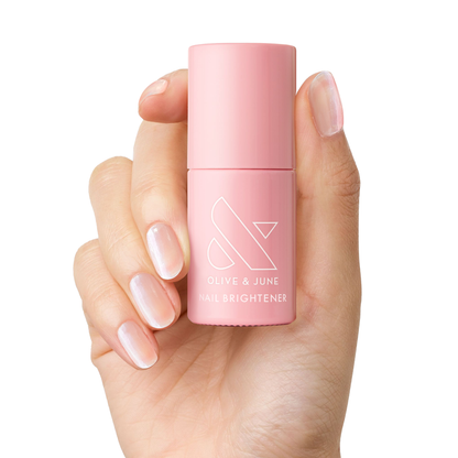 Hand holding pink bottle of The Nail Brightener by Olive and June for brightening stained nails and at-home mani care