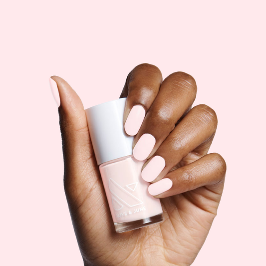 Hand with smooth nails painted in creamy pink PINK SANDS polish by Olive and June holding the bottle against pink background