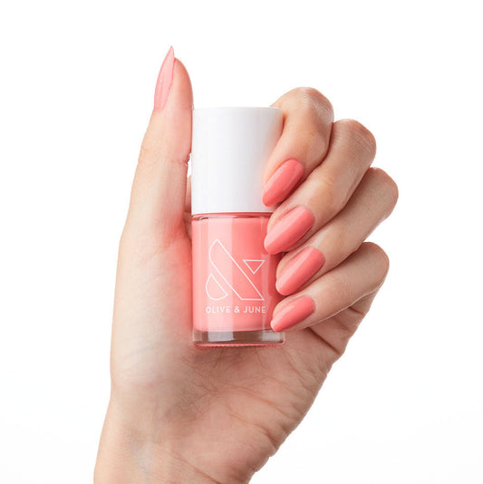 Hand with nails polished in Stinson Sunset gel polish by Olive and June holding matching nail polish bottle